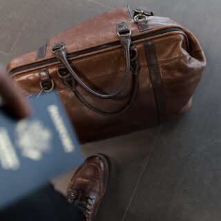 man holding passport with bag at his feet