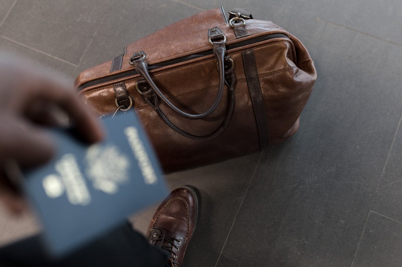man holding passport with bag at his feet