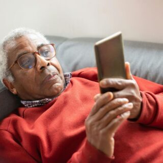 An elderly man using his cell phone at home.