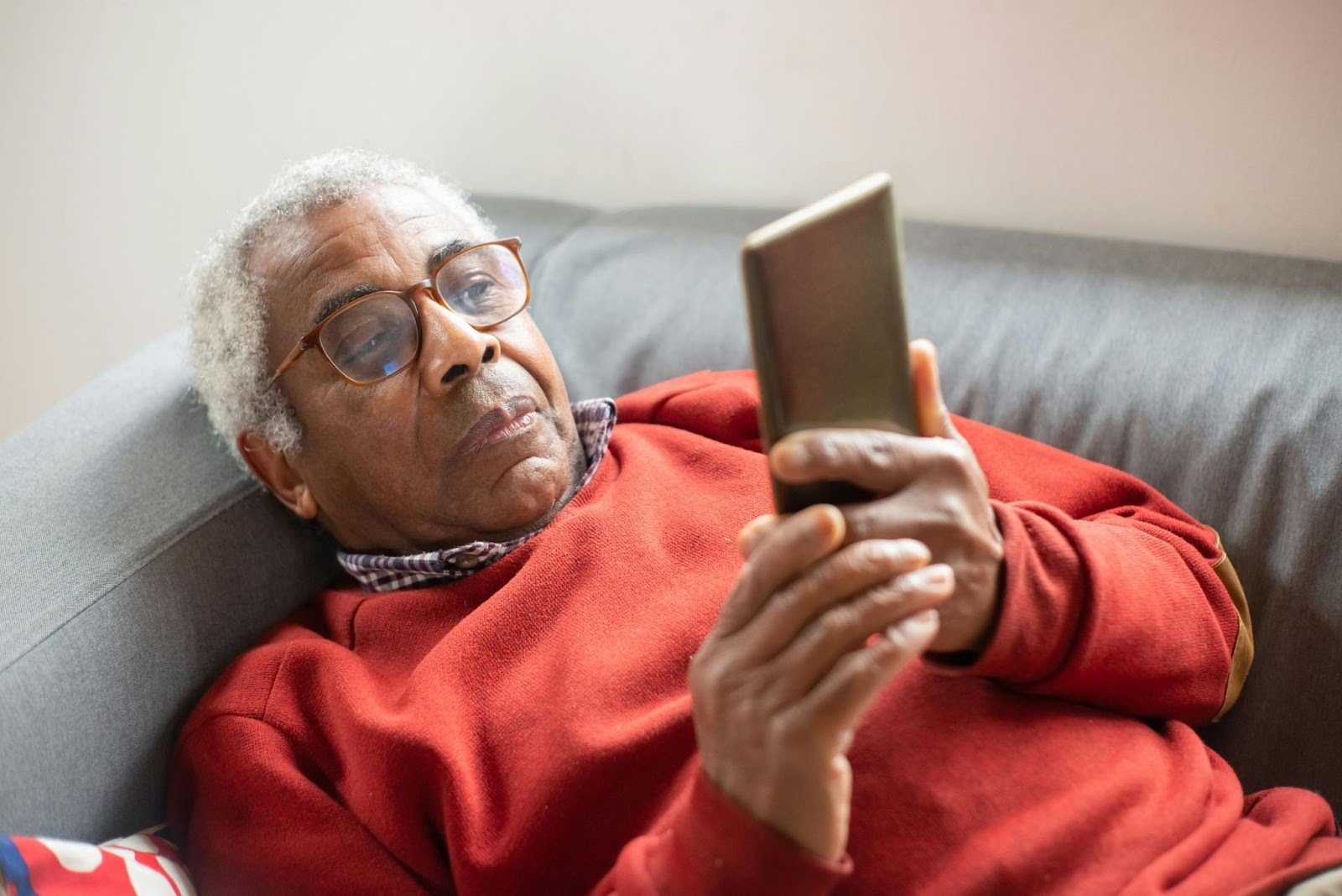 An elderly man using his cell phone at home.
